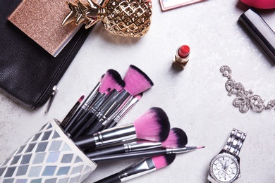 Photo of Holder with professional brushes, makeup products and accessories on light background, top view