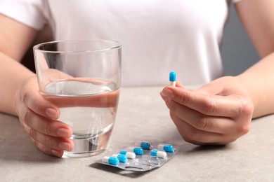 Woman with pills and glass of water at grey table, closeup