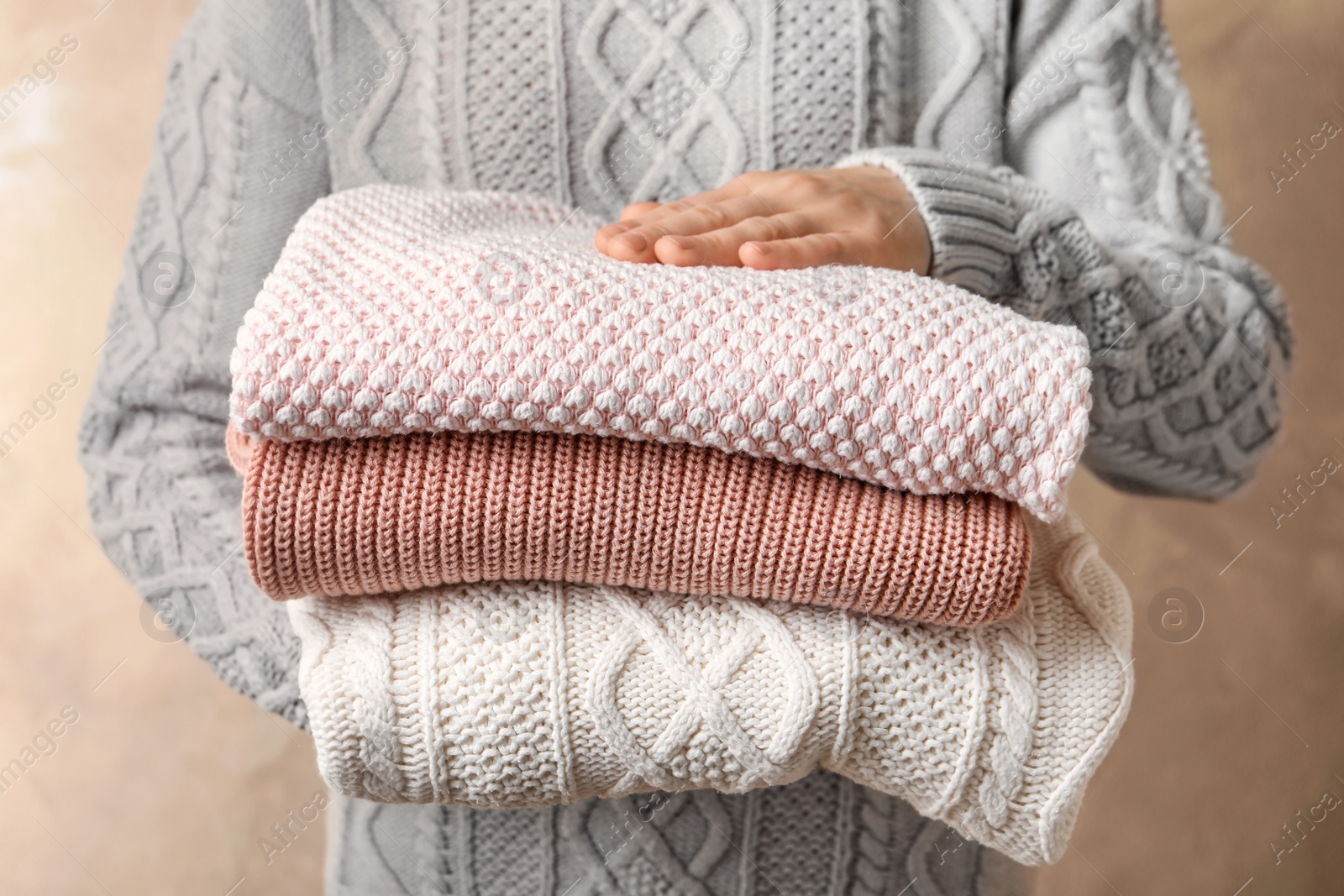 Photo of Young woman holding stack of warm knitted clothes, closeup