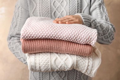 Photo of Young woman holding stack of warm knitted clothes, closeup