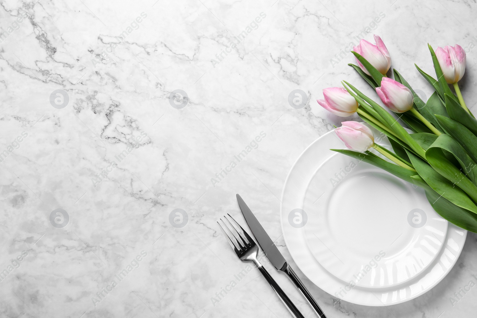 Photo of Stylish table setting with cutlery and tulips on white marble background, flat lay. Space for text