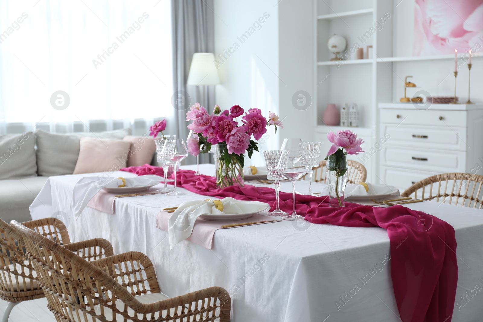 Photo of Beautiful table setting with pink accent and rattan chairs in dining room