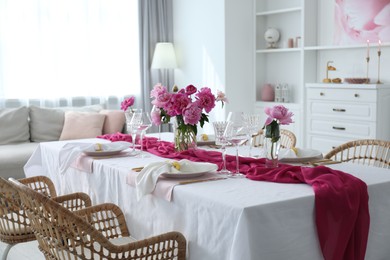 Photo of Beautiful table setting with pink accent and rattan chairs in dining room