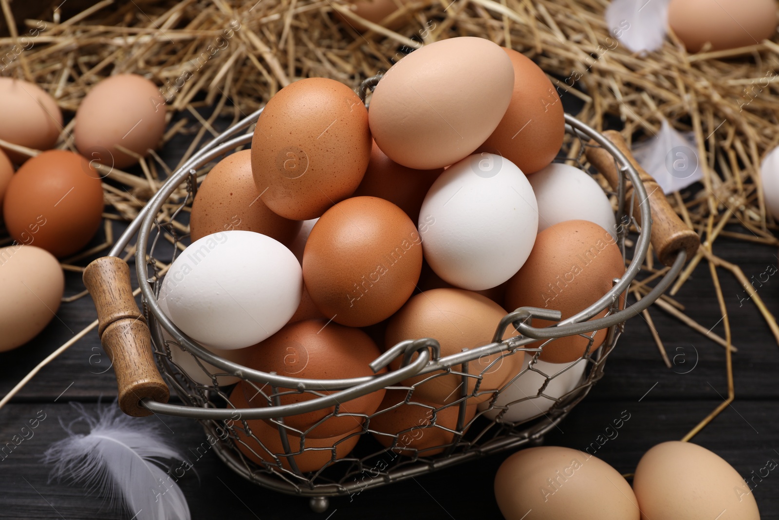 Photo of Fresh chicken eggs and dried straw on black wooden table, closeup