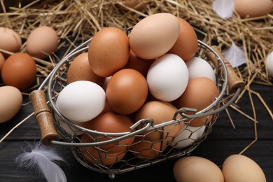 Fresh chicken eggs and dried straw on black wooden table, closeup