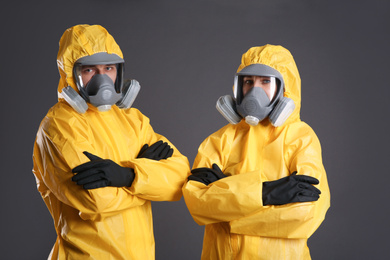 Man and woman wearing chemical protective suits on grey background. Virus research