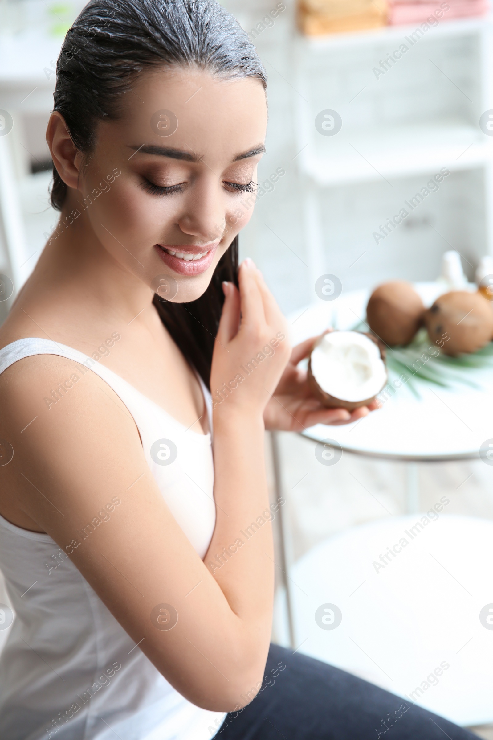 Photo of Young woman applying coconut oil onto hair at home