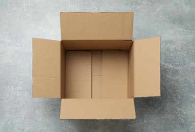 Photo of Empty open cardboard box on grey table, top view