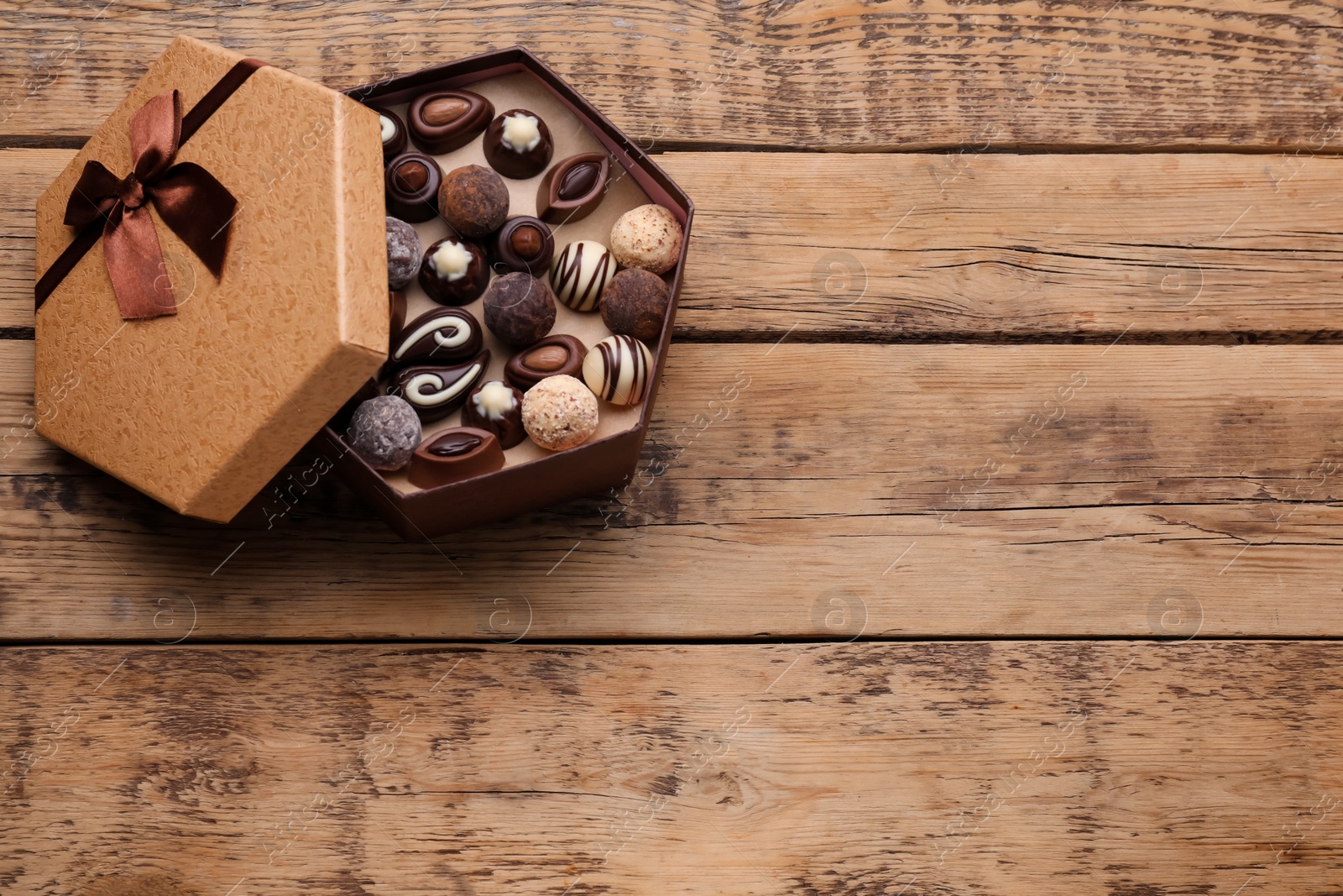 Photo of Open box of delicious chocolate candies on wooden table, top view, Space for text