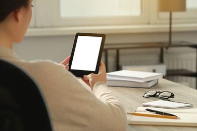 Young woman using e-book reader at wooden table indoors, closeup