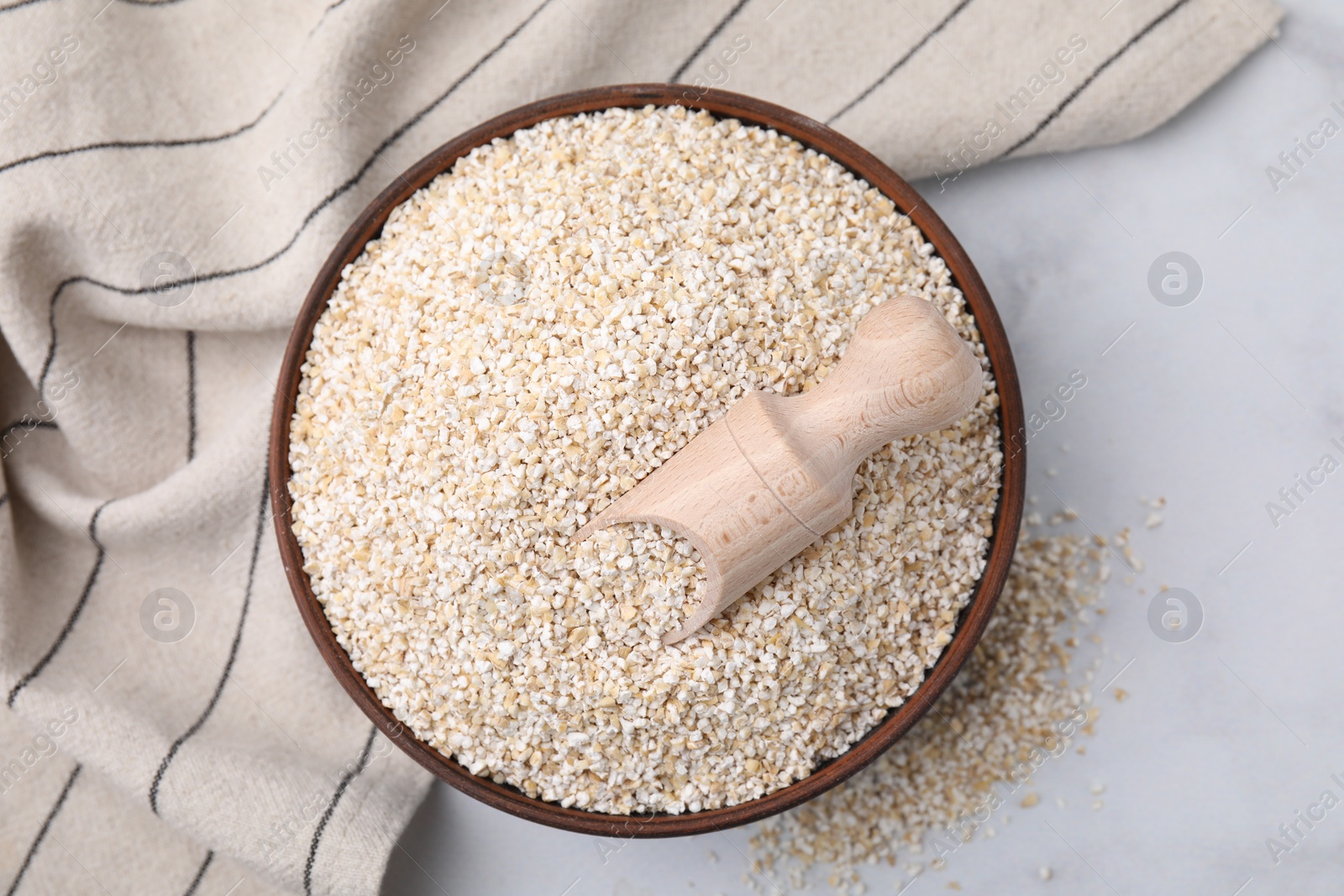 Photo of Dry barley groats and scoop in bowl on white table, top view