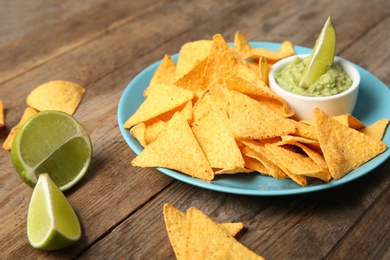Photo of Plate with delicious mexican nachos chips, guacamole sauce and lime on wooden table