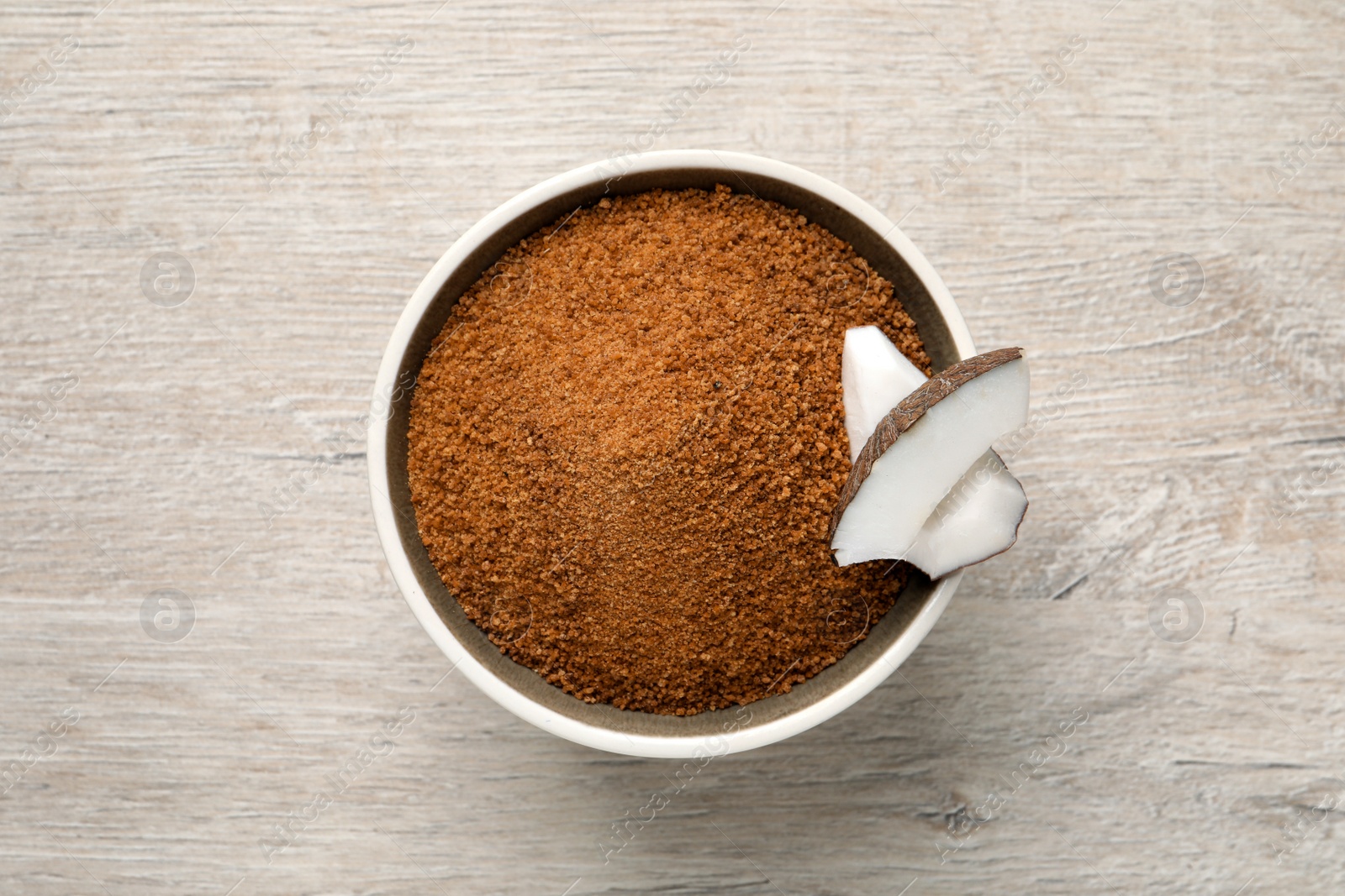 Photo of Natural coconut sugar in bowl on white wooden table, top view