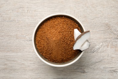 Natural coconut sugar in bowl on white wooden table, top view