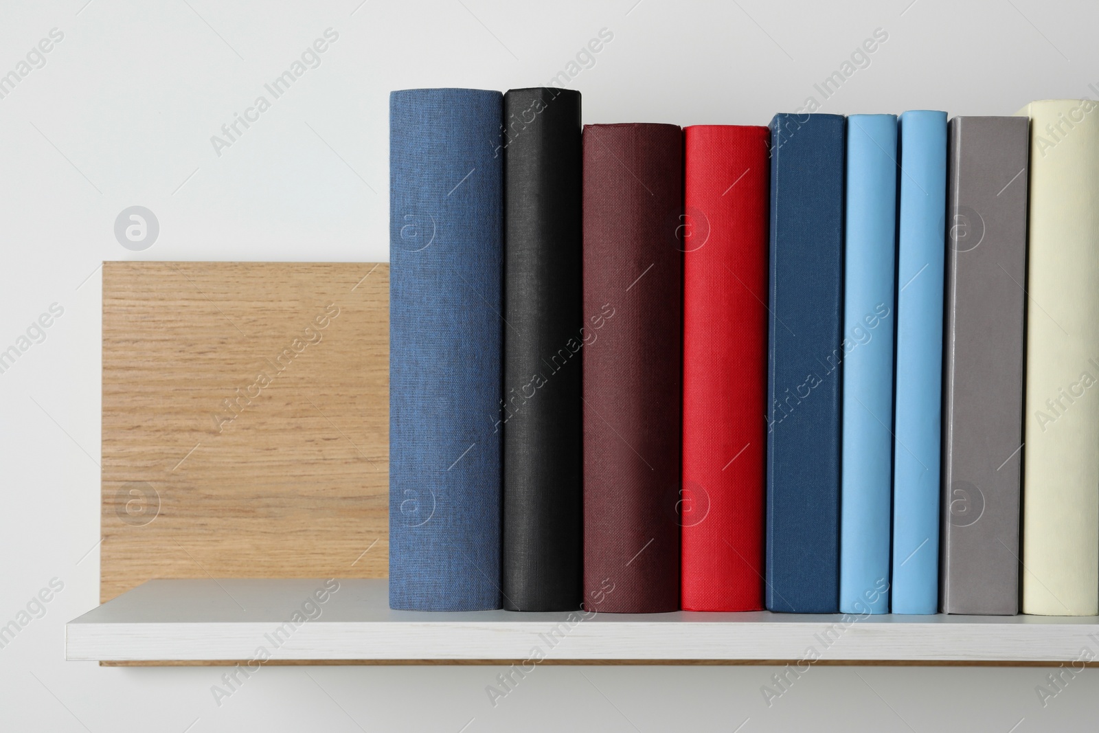 Photo of Many hardcover books on wooden shelf near white wall