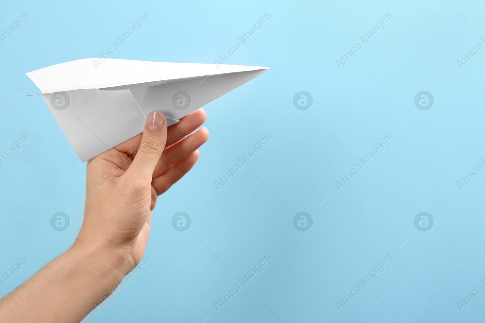 Photo of Woman holding paper plane on light blue background, closeup. Space for text