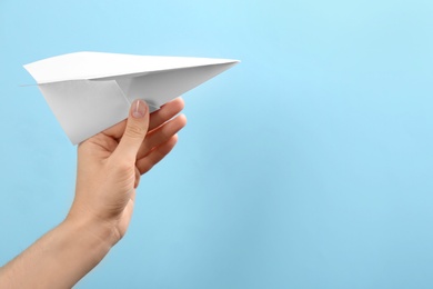 Photo of Woman holding paper plane on light blue background, closeup. Space for text