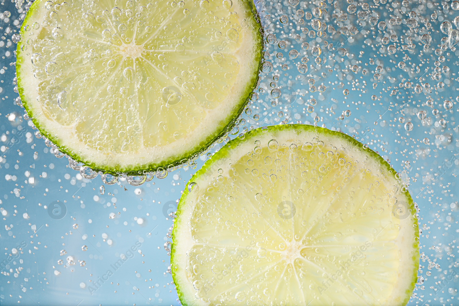 Photo of Juicy lime slices in soda water against light blue background, closeup