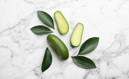 Photo of Fresh seedless avocados with green leaves on marble table, flat lay