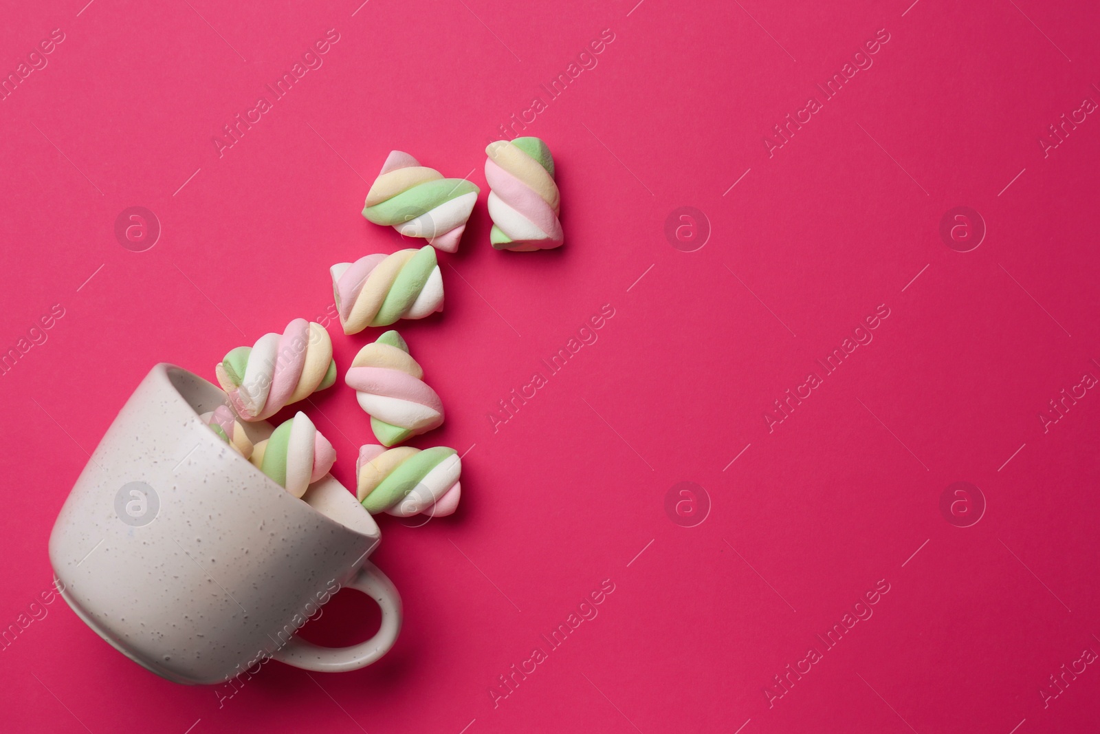 Photo of Overturned cup with delicious colorful marshmallows on crimson background, flat lay. Space for text