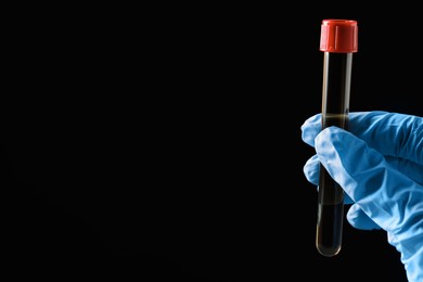 Photo of Scientist holding test tube with liquid on black background, closeup. Space for text