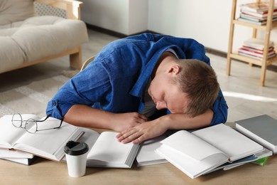 Photo of Tired man sleeping near books at wooden table in room