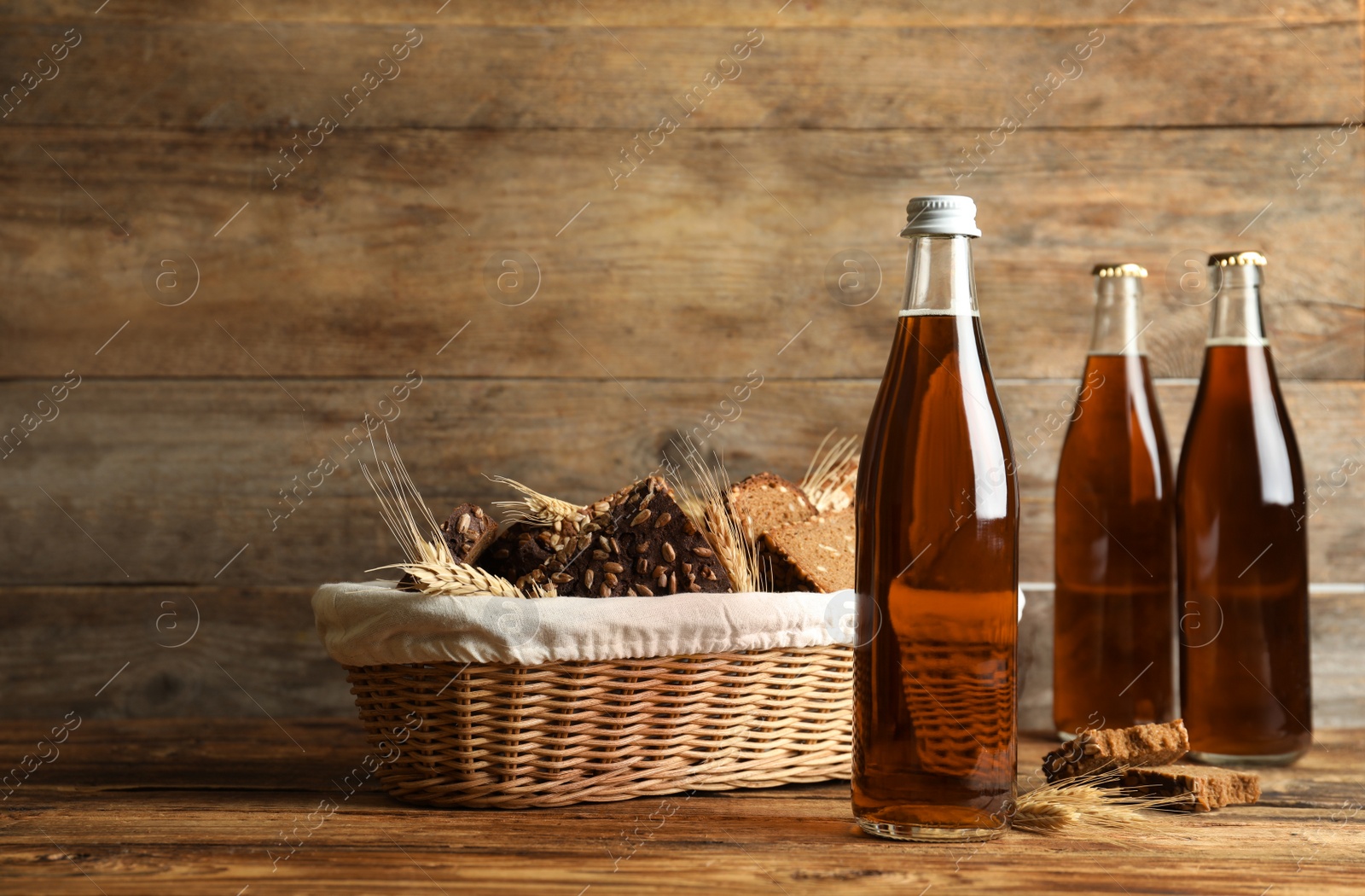 Photo of Bottles of delicious fresh kvass, spikelets and bread on wooden table