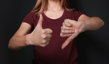 Photo of Woman showing THUMB UP and DOWN gesture in sign language on black background, closeup