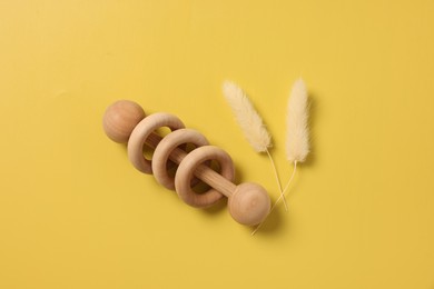 Baby accessory. Wooden rattle and dry spikes on yellow background, top view