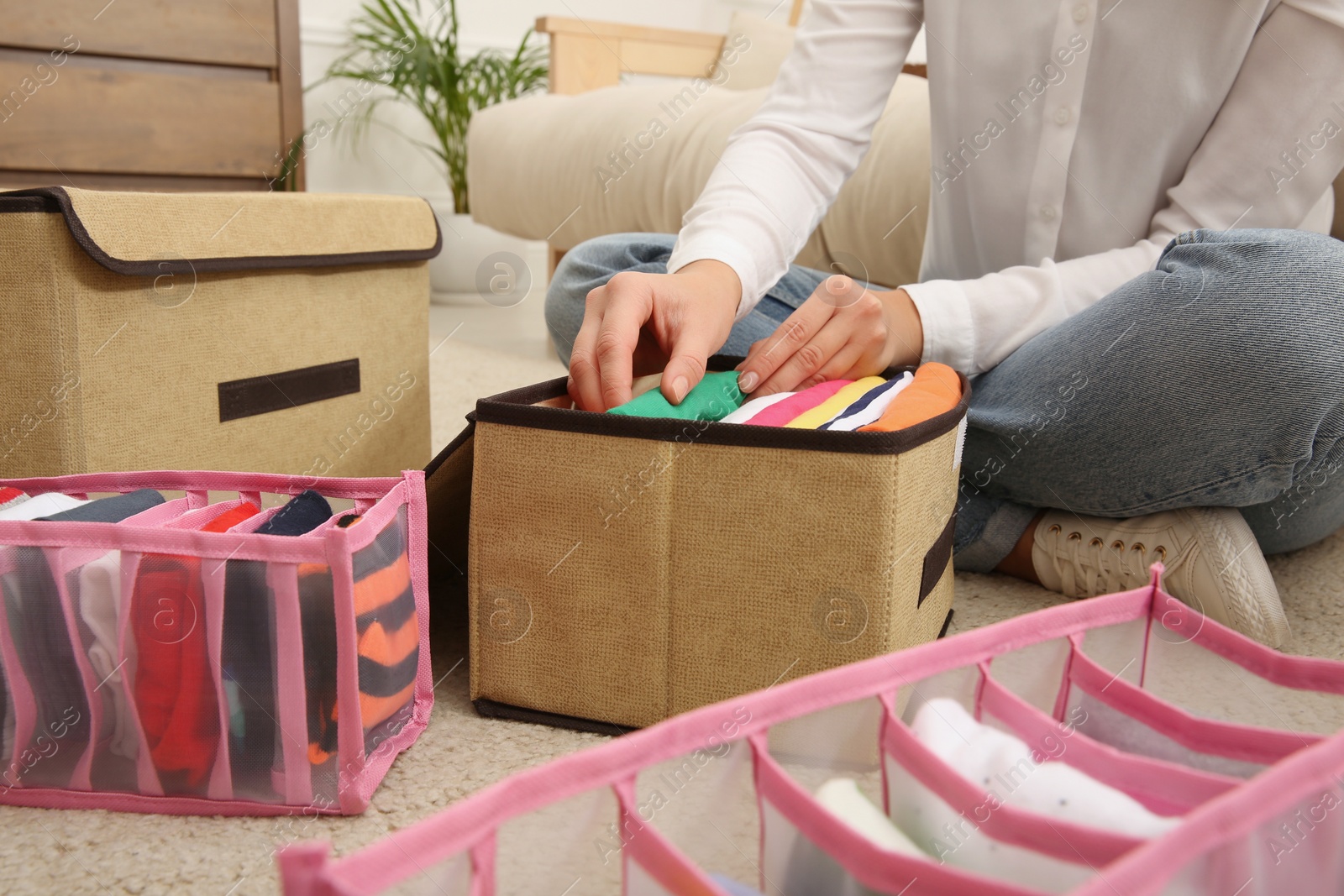 Photo of Woman folding clothes on floor at home, closeup. Japanese storage system