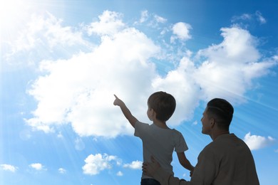 Image of Godparent with child pointing at blue sky with white clouds