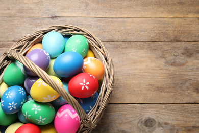 Basket with Easter eggs on wooden table, top view. Space for text