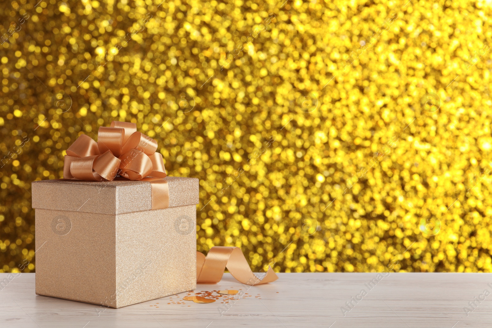 Image of Beautiful gift box on white wooden table against shiny golden background, bokeh effect. Space for text