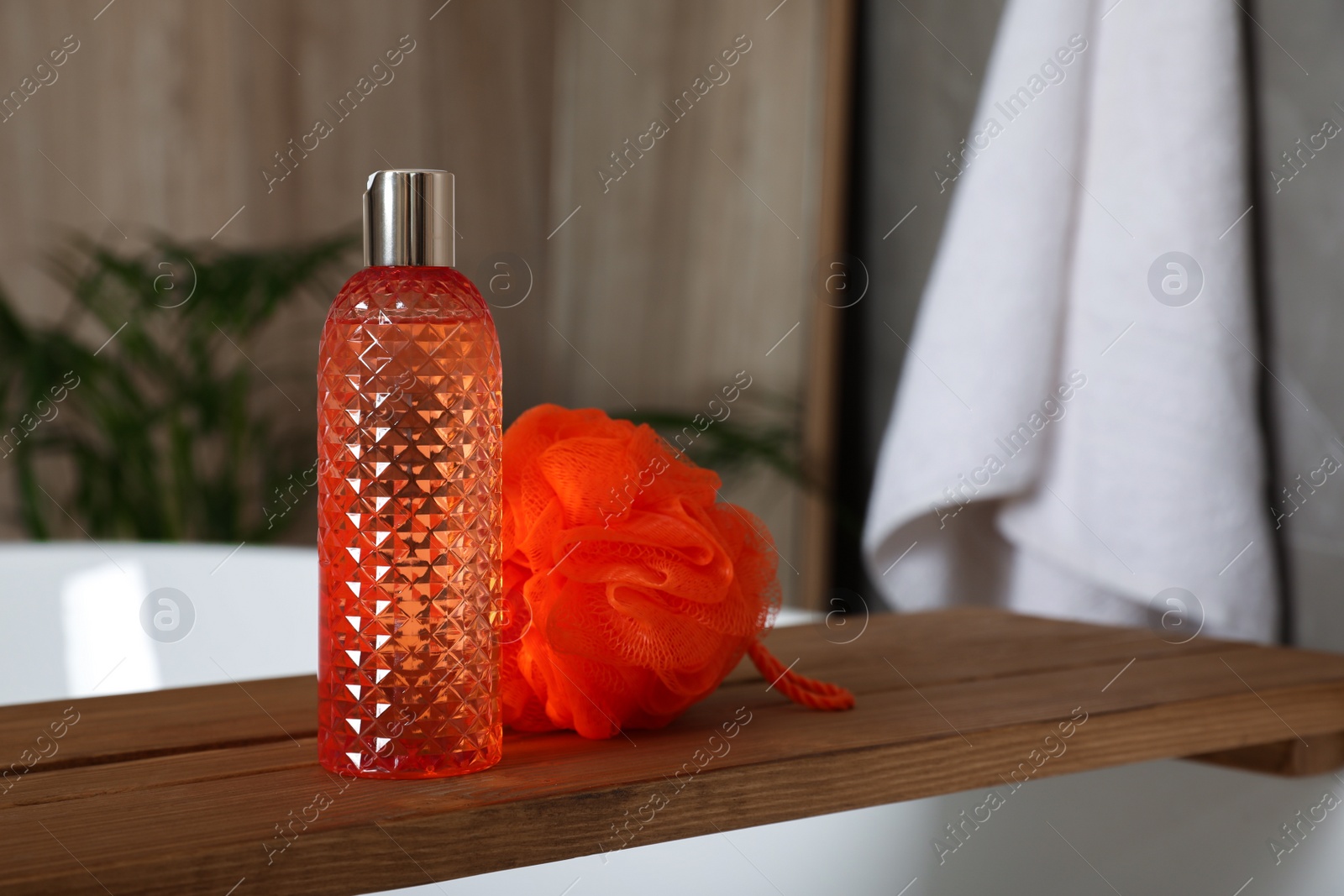 Photo of Wooden bath tray with bottle of shower gel and mesh pouf on tub indoors, space for text