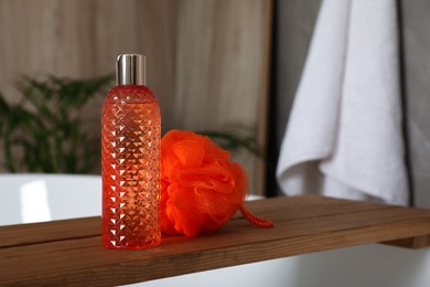 Wooden bath tray with bottle of shower gel and mesh pouf on tub indoors, space for text