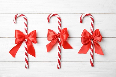 Photo of Flat lay composition of tasty candy canes with bows on wooden background