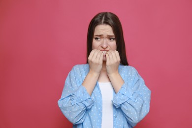 Photo of Young woman biting her nails on pink background