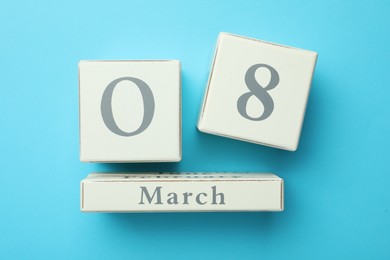 Photo of Wooden block calendar with date 8th of March on light blue background, flat lay. International Women's Day