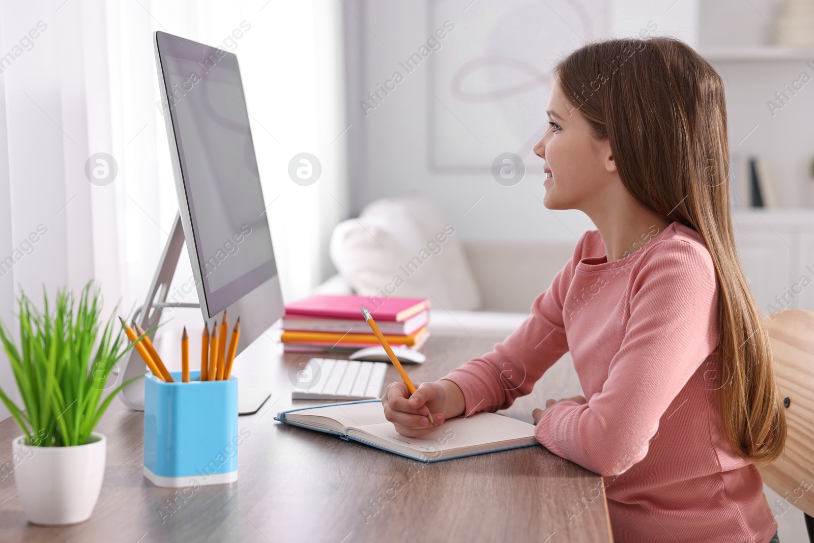 Photo of E-learning. Cute girl taking notes during online lesson at table indoors