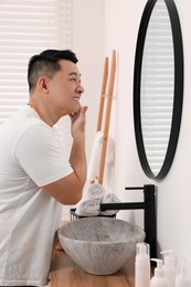 Photo of Handsome man applying cream onto his face near mirror in bathroom