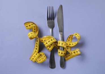 Photo of Cutlery with measuring tape on light purple background, flat lay. Diet concept