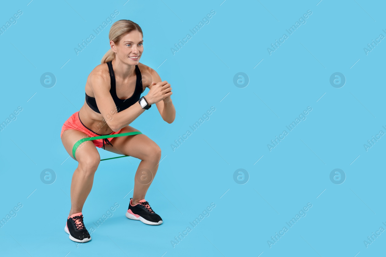 Photo of Woman exercising with elastic resistance band on light blue background. Space for text