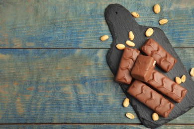 Photo of Slate board of chocolate bars with nuts on light blue wooden table, top view. Space for text