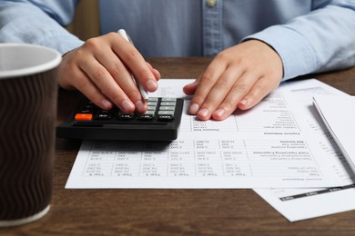 Woman working with data using calculator at wooden table, closeup