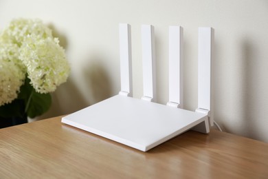 Photo of New modern Wi-Fi router on wooden table near white wall