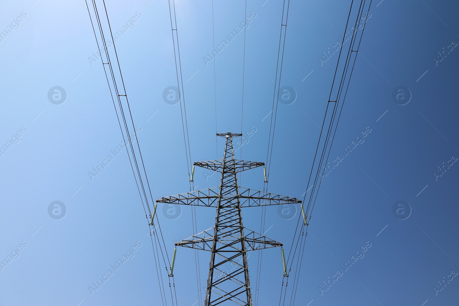 Photo of High voltage tower with electricity transmission power lines against blue sky, low angle view