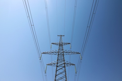 Photo of High voltage tower with electricity transmission power lines against blue sky, low angle view
