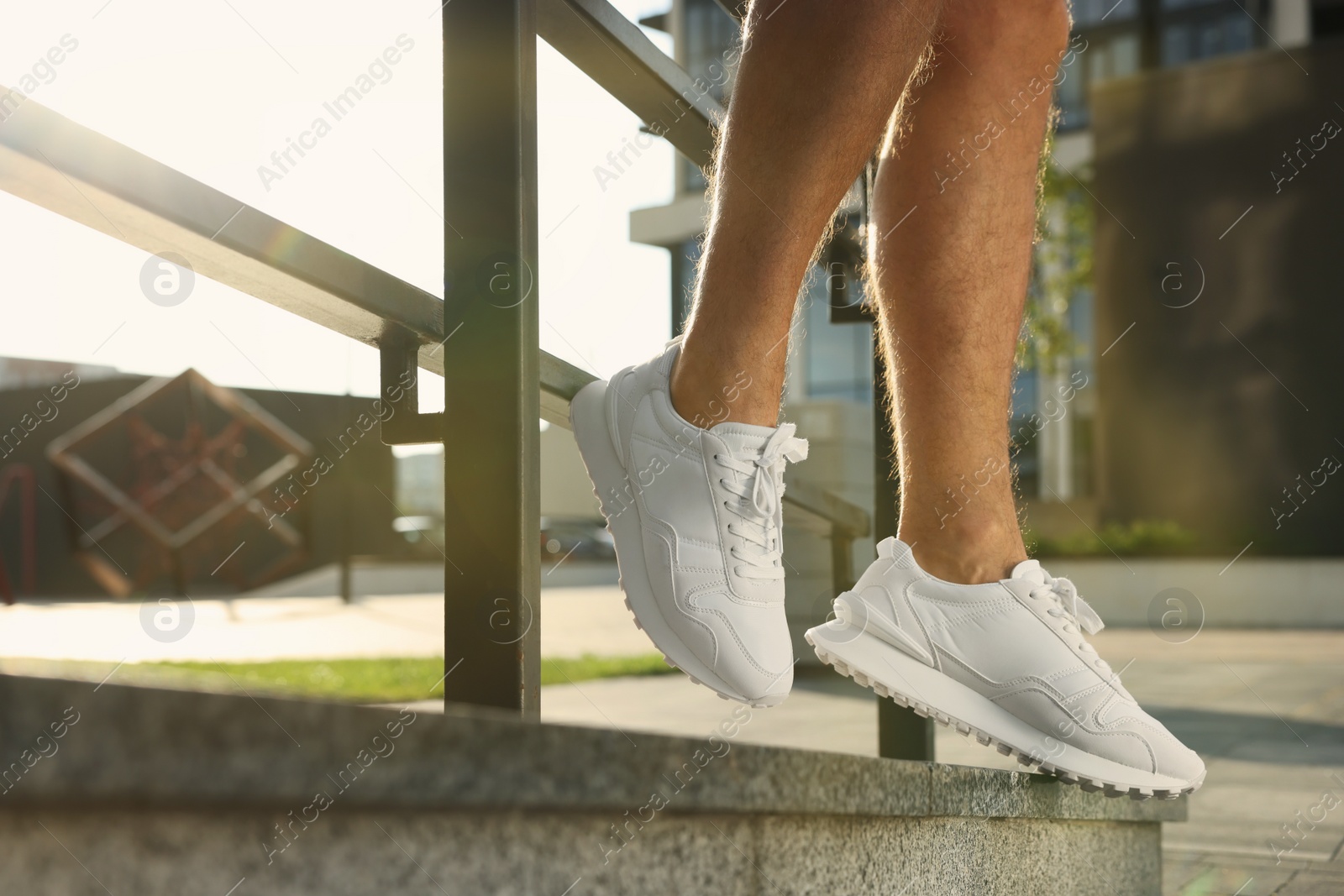 Photo of Man in stylish sneakers sitting on railing outdoors, closeup