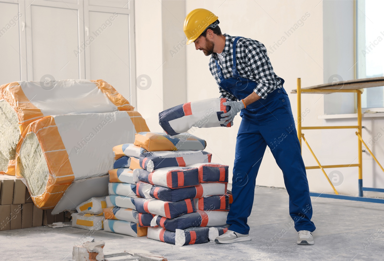 Photo of Professional builder in uniform with bag of cement indoors