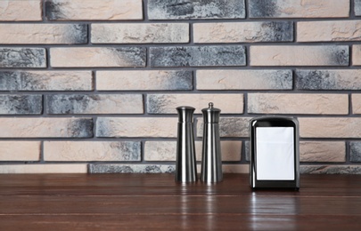 Napkin holder with salt and pepper shakers on table against brick wall. Space for text